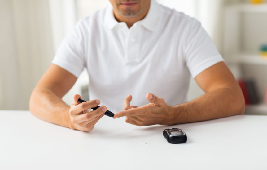close up of man checking blood sugar level by glucometer at home